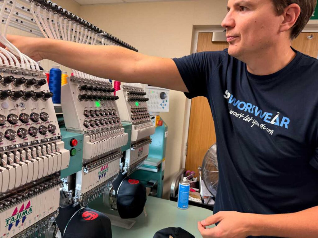 Man operating embroidery machines in a workshop, adjusting thread spools.