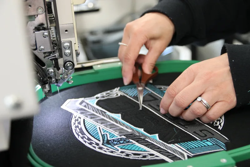 Trimming threads by hand on a large embroidered back logo, still in the hoop on the machine