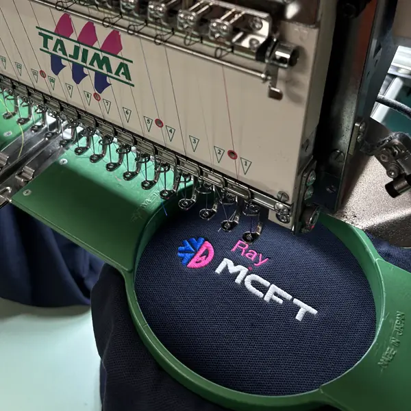 A logo and name being embroidered onto a polo shirt on one of our Tajima embroidery machines